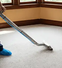 Steam carpet cleaning technician using a hot-water extraction wand on a residential carpet, wearing blue protective shoe covers San Jose, CA.