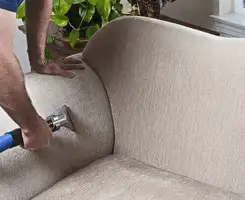 Professional upholstery cleaner deep-cleaning a fabric sofa with a handheld extraction tool and hose in San Jose, CA.